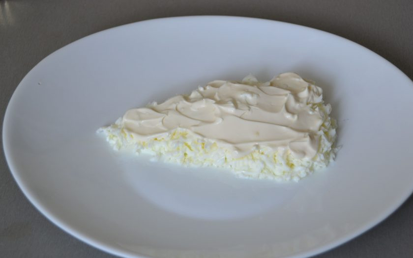1. Этап. Салат Сырный ломтик на год Крысы: Отделите белки вареных куриных яиц, натрите на терке, выложите на тарелку в форме треугольника, сверху нанесите майонез.