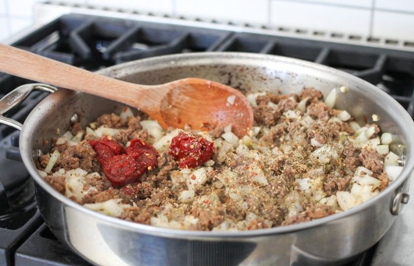 1. Этап. Вкусная лазанья: Как только мясо станет коричневатого оттенка, добавьте в него лук с чесноком, томатную пасту и итальянские травы.