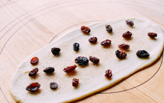 1. Этап. Булочки Розы с изюмом: 1. В чашу миксера вылейте сливки, молоко, сахар (1/3 стакана), 1 яйцо, муку, дрожжи и соль, смешайте все ингредиенты в течение 15 минут, затем накройте тесто полотенцем и оставьте на 1-1,5 часа. Обомните тесто руками и разделите его на 12 частей. Каждую часть раскатайте в тонкий овал, посыпьте корицей, сахаром и изюмом.