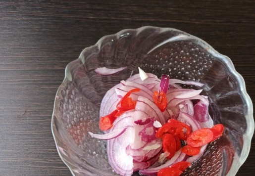 1. Этап. Чизбургер с копченой рулькой и соусом Спайси: Лук тонко нарезать перьями и смешать с колечками чили. Посолить, добавить щепотку сахара и слегка всё помять пальцами. Солёный огурец нарезать ломтиками.