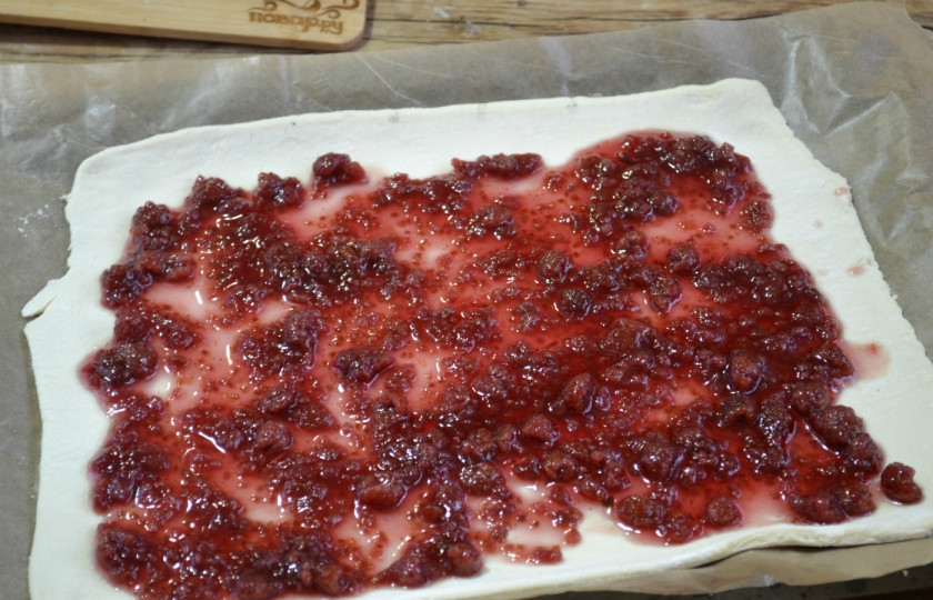 1. Этап. Пирог с малиной из слоеного теста: Лист теста раскатайте тонко, выложите на противень, застеленный бумагой для выпекания. Выложите консервированную малину.