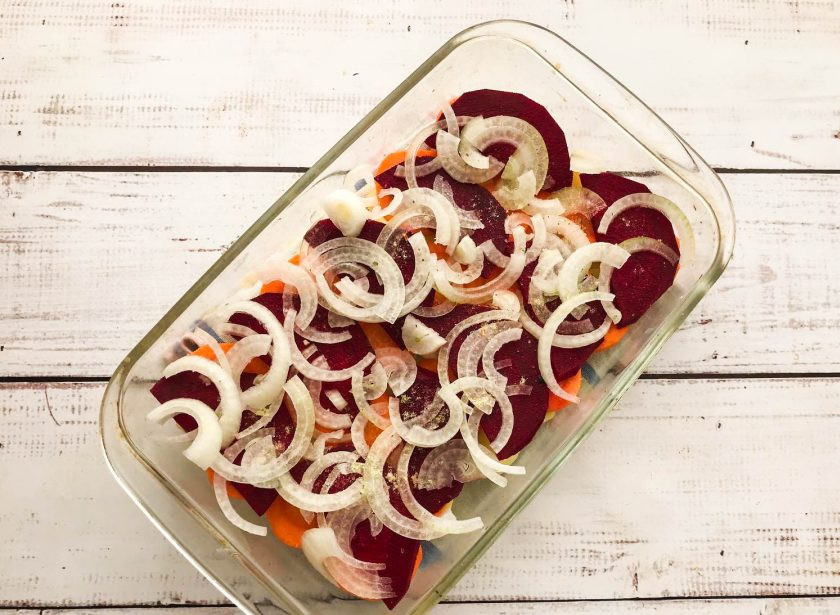 1. Этап. Печеный картофель со свеклой: Лук очистите от шелухи, нарежьте полукольцами и выложите поверх овощей. Посолите, добавьте специи и отправьте в предварительно разогретую до 180 градусов духовку на 35-40 минут.