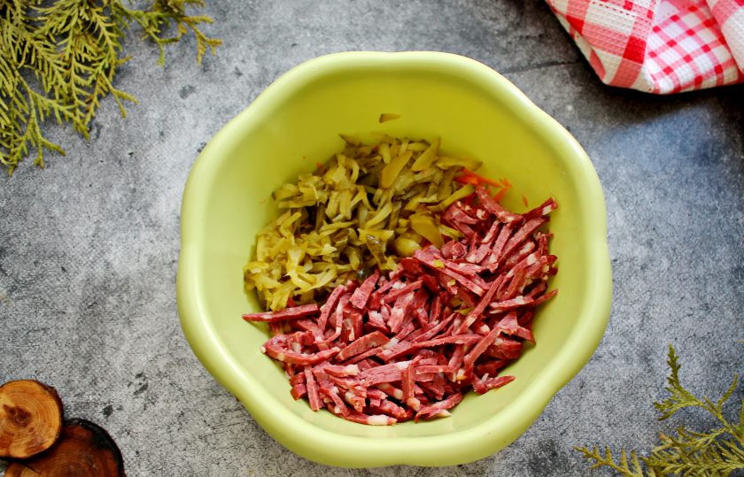 1. Этап. Салат Гнездо глухаря с колбасой: Маринованные огурцы и колбасу порежьте соломкой и добавьте в салат.