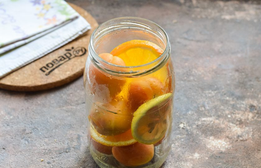 1. Этап. Фанта из абрикосов на зиму: Банку для заготовки тщательно вымойте с пищевой содой, после ополосните хорошо под теплой проточной водой. Стерилизуйте банку и крышку удобным способом – над паром, в духовке или микроволновке. После переложите в банку абрикосы, лимон, апельсин.