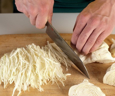 1. Этап. Маринованная капуста с клюквой: 1. Очистите капусту от верхних листьев и нарежьте на 4-6 частей в зависимости от размера. Затем острым ножом нашинкуйте и выложите в глубокую мисочку. При желании можно натереть капусту на шинковке, однако не слишком мелко, чтобы маринованная капуста с клюквой в домашних условиях оставалась хрустящей.