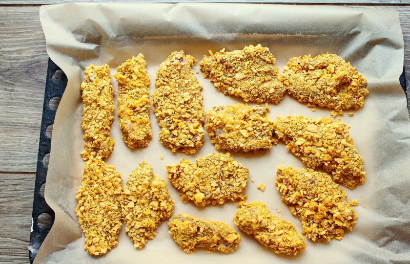 1. Этап. Куриные нагетсы в кукурузной панировке в духовке: Противень застелите пергаментом для выпечки и выложите нагетсы в один слой.