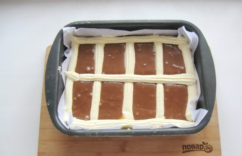 1. Этап. Пирог Стеганое одеяло: Форму для выпечки застелите пекарской бумагой. Выложите темное тесто. Затем с помощью кулинарного мешка с насадкой отсадите белое тесто, образуя квадраты.