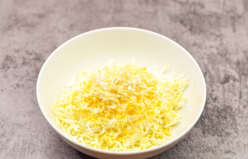 1. Этап. Рулет из баклажан, яиц и ветчины: Тертый твердый сыр переложите в миску. Туда же натрите на мелкой терке куриные яйца и чеснок.