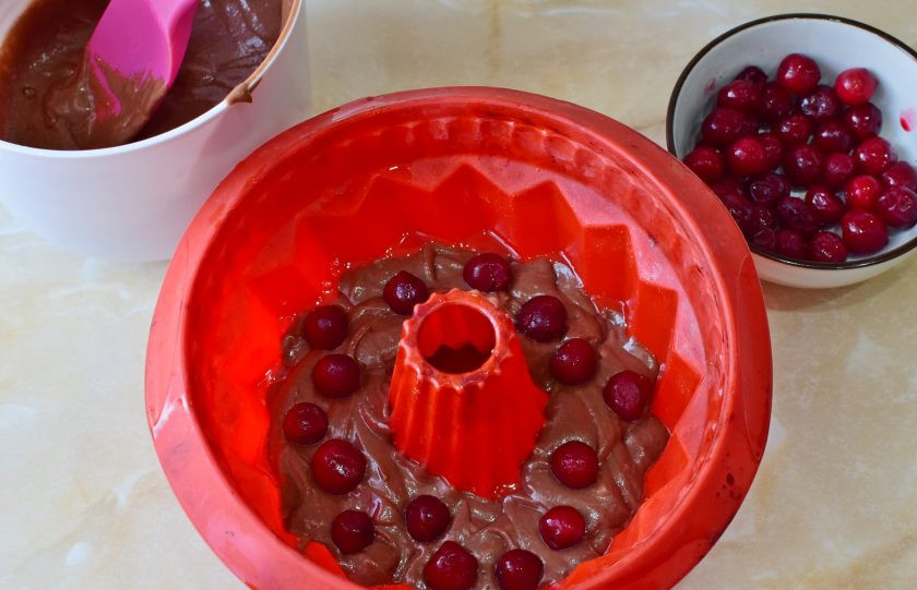 1. Этап. Кекс с вишней в микроволновке: Для выпечки можно взять форму из силикона или стекла. Смажьте её растительным маслом и выложите половину теста. Добавьте вишню.