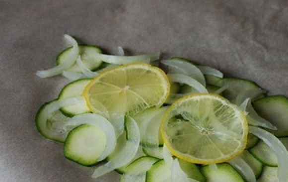 1. Этап. Запечённая семга с цуккини и луком: Возьмите четыре куска пергамента для запекания и выложите не него цуккини, затем — ломтики лука. Мелко порежьте масло, выложите его на овощи. Также положите сверху по несколько кружочков лимона.