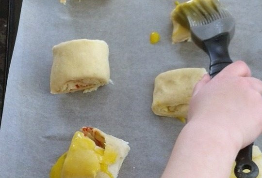 1. Этап. Булочки-рулеты с сырной начинкой: 4. Сверните пласт в рулетик и разрежьте на части, каждую часть смажьте куриным желтком.