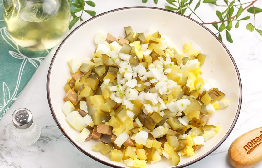 1. Этап. Салат из печени баранины: Нарежьте соленые огурцы мелкими кубиками, отжав из нарезки рассол. Мелко нарежьте репчатый лук и добавьте оба ингредиента в емкость. По желанию репчатый лук можно заменить зеленым или красным.