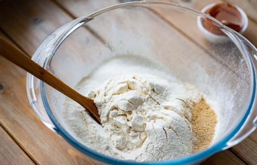 1. Этап. Вареники на кефире и дрожжах: Просейте в отдельную сухую миску муку, к ней добавьте сухие дрожжи и сахар (25 грамм). Перемешайте эти сухие ингредиенты ложкой до равномерного их распределения по массе.