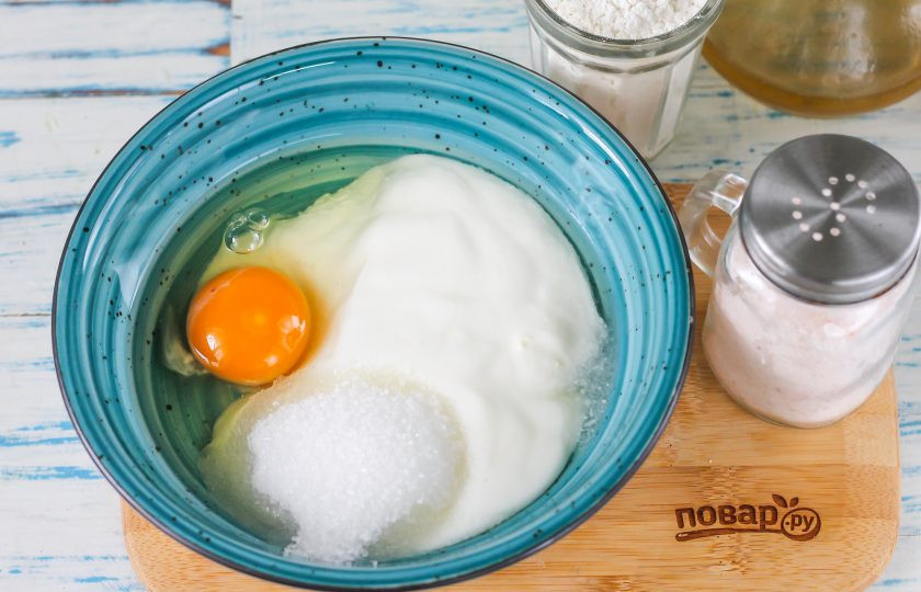 1. Этап. Оладьи в мультиварке: Кефир перелейте в глубокую емкость, вбейте туда же куриное яйцо. Всыпьте соль и сахарный песок. Тщательно взбейте все содержимое венчиком или вилкой.