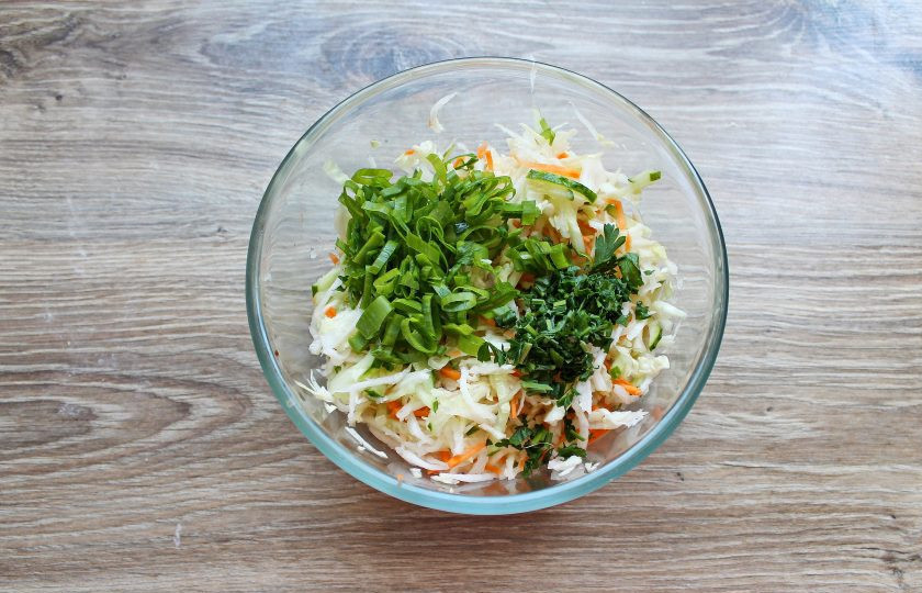 1. Этап. Салат с капустой и дайконом: Петрушку и зеленый лук порежьте, выложите в миску с овощами и перемешайте.