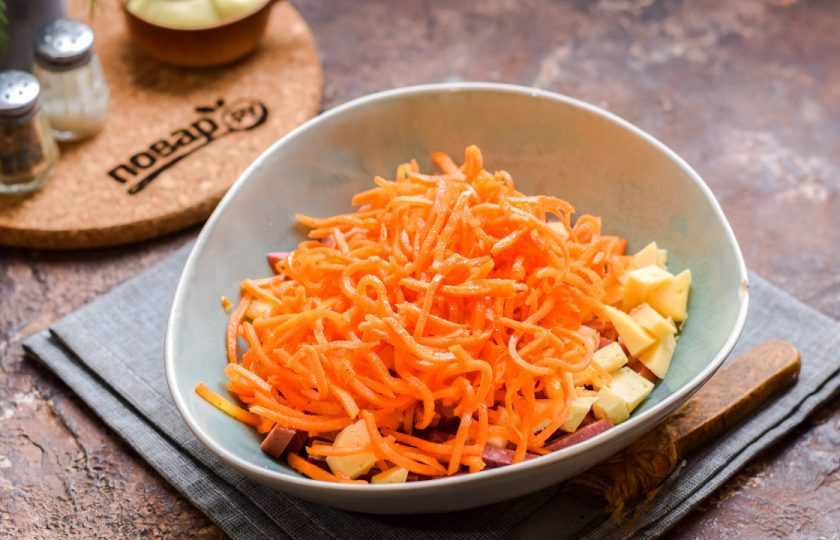 1. Этап. Салат Мужской каприз с колбасой: Переложите сыр и колбасу в салатник. Также добавьте в салат морковь по-корейски. Если морковь длинная, ее лучше немного нарезать.