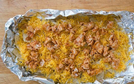 1. Этап. Куриные начос: 3. Посыпьте чипсы тертым на средней или крупной терке сыром (оставьте немного), полейте ¼ стакана соусом «Барбекю», распределите поверх куриное мясо, нарезанное небольшими кусочками и посыпьте оставшимся сыром.
