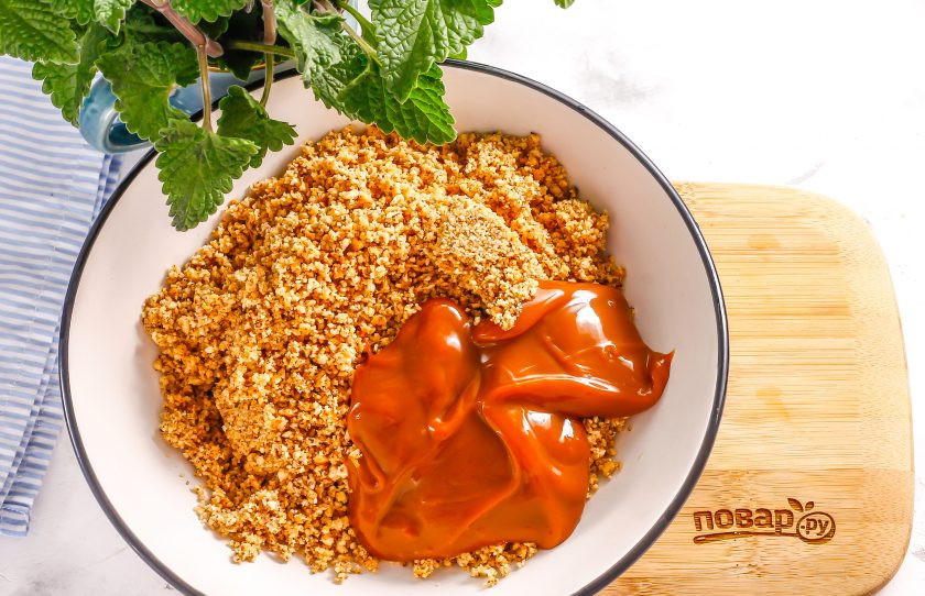 1. Этап. Постное пирожное Картошка: Пересыпьте приготовленную крошку в глубокую емкость, выложите туда же вареное сгущенное молоко. Аккуратно все перемешайте и оставьте на 20 минут, чтобы крошка печенья слегка разбухла.