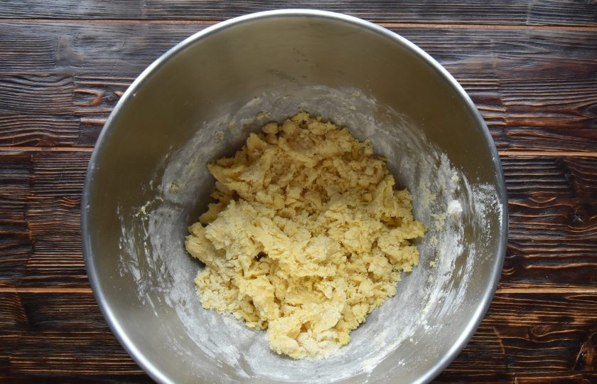 1. Этап. Пирог Ложный сырник: Когда мука впитает в себя влагу, разотрите тесто лопаткой до состояния крошки. Выложите заготовку песочного теста на столешницу и соберите крошку в шар.