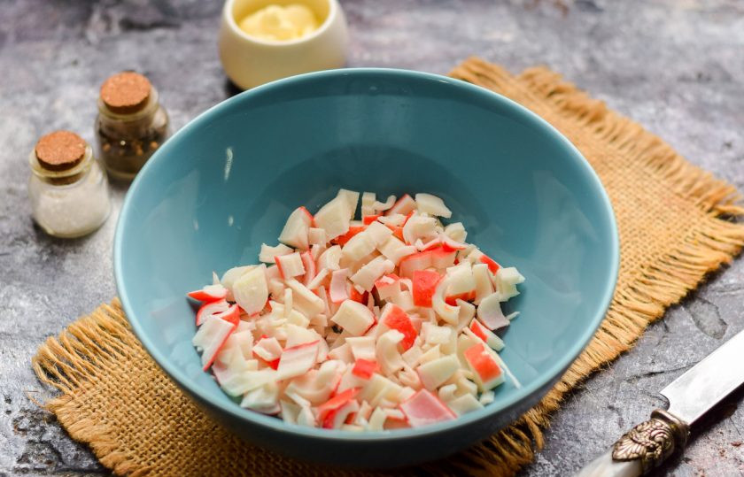 1. Этап. Салат с кукурузой, авокадо и крабовыми палочками: Крабовые палочки заранее разморозьте, после нарежьте небольшими кубиками, сложите в салатник.