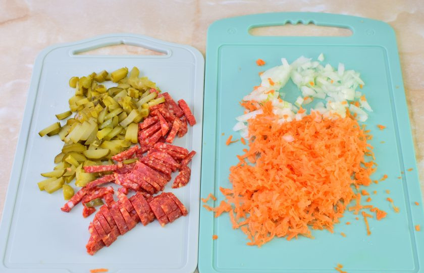 1. Этап. Рассольник с рисом и колбасой: В это время подготовьте овощи. Морковь потрите на терке, а лук мелко нарежьте. Нарежьте соломкой соленые огурцы и колбасу.