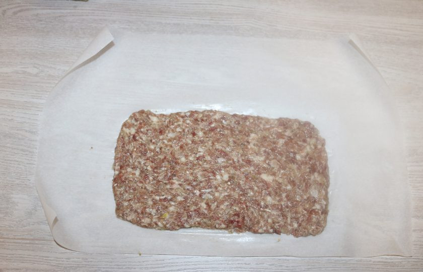1. Этап. Мясной рулет с ананасами: На лист пекарской бумаги выложите фарш равномерно тонким слоем в виде прямоугольника.
