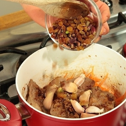 1. Этап. Афганский плов: Далее выкладываем обжаренный лук, изюм, орехи (лучше всего очищенные фисташки) и чеснок (целые зубчики).