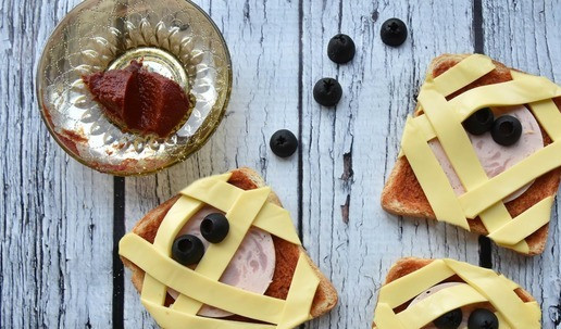 1. Этап. Тосты для друзей на хэллоуин: На подсушенный тост нанесите 1 столовую ложку томатного соуса и распределите по всей поверхности тонким слоем, излишки уберите. Положите на середину ломтик колбасы из индейки. В хаотичном порядке выложите полосочки сыра, имитирующие 