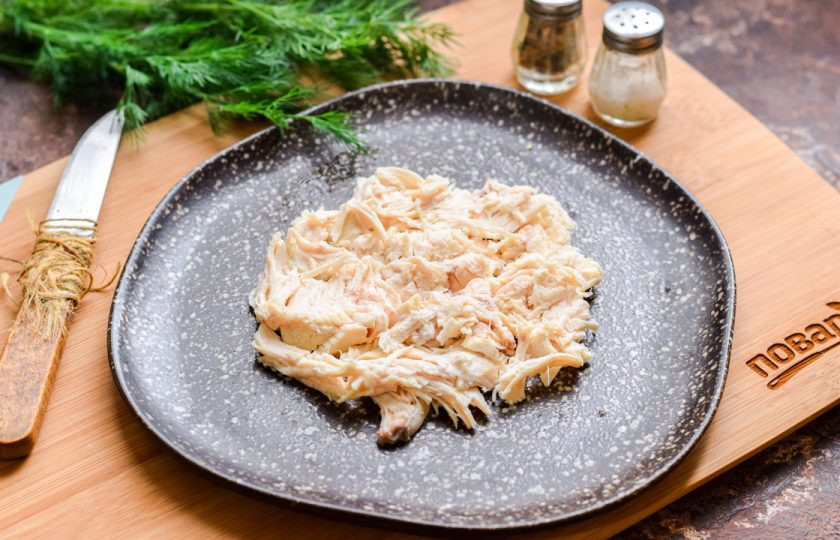 1. Этап. Слоеный салат с курицей Бычок: Куриное филе нарежьте небольшими кусочками или разберите на волокна. Подготовьте плоскую тарелку для салата, выложите курицу первым слоем, в виде круга — как показано на фото.