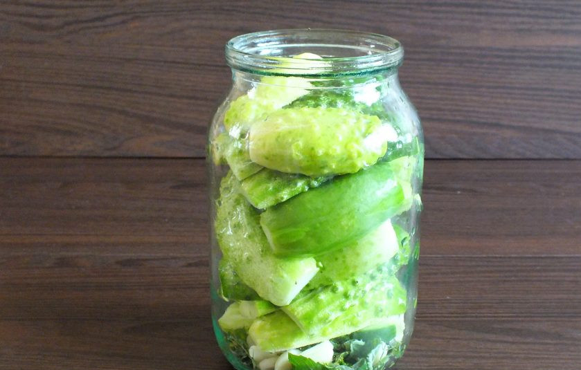 1. Этап. Малосольные огурцы с мятой и чесноком: Огурцы разрежьте вдоль на две половинки. Заполните ими банку, добавьте нарезанный чеснок.