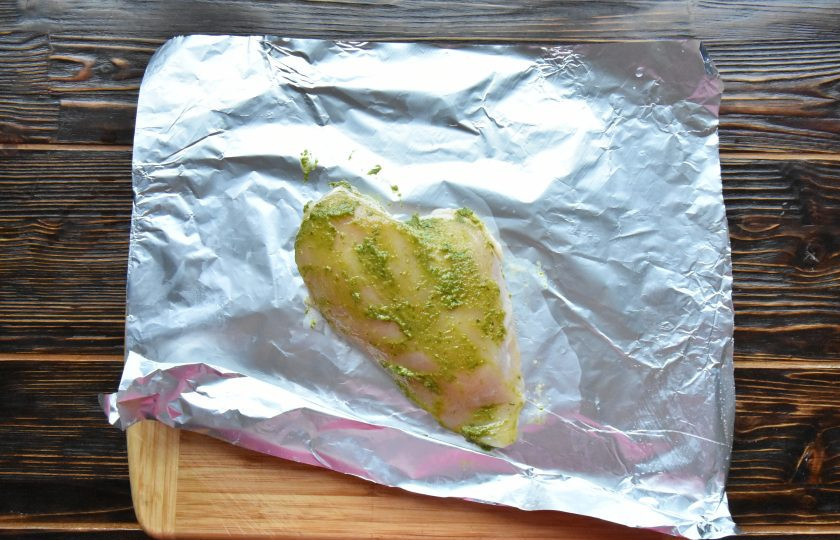 1. Этап. Пицца с курицей и соусом песто: Филе куриной грудки замаринуйте в соусе песто. Добавьте соль и молотый перец по вкусу. Заверните филе в фольгу и запеките до готовности в духовке, разогретой до 200 градусов в течение 20-25 минут.