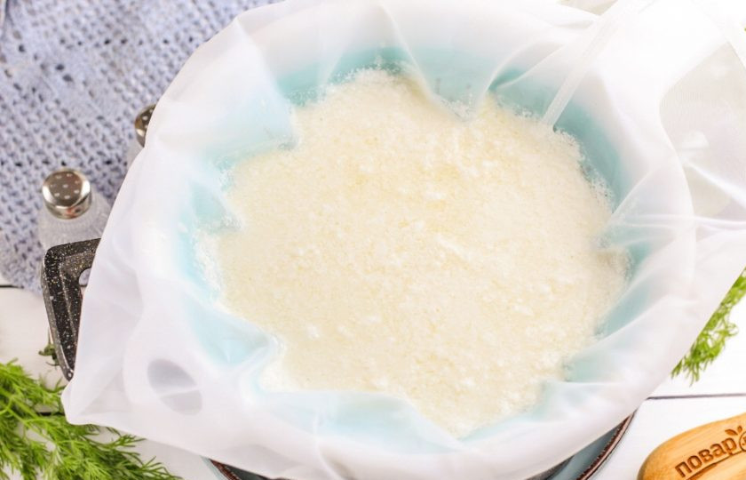 1. Этап. Сыр адыгейский: Застелите дуршлаг марлей в два слоя или специальным пакетом для приготовления сыра. Перелейте в него горячую массу — сыворотка сольется, а сырная масса останется в пакете.