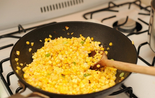 1. Этап. Салат с жареными грибами и кукурузой: 4. Срежьте с початков зерна кукурузы. На отдельной сковороде разогрейте немного масла. Выложите туда немного лука (белая часть от перьев зеленого лука) и обжарьте буквально минутку. После добавьте зерна кукурузы и на среднем огне, помешивая, томите минут 5-7.