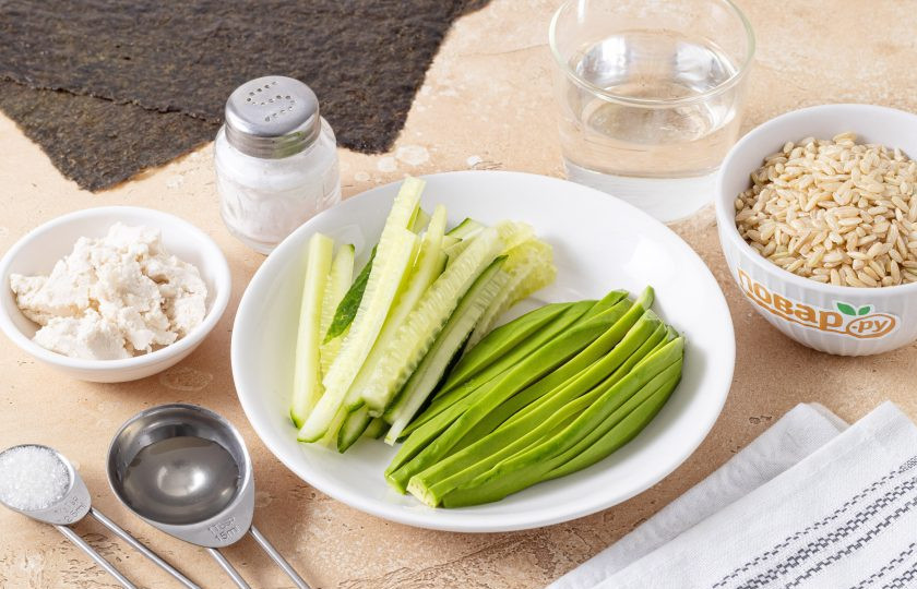 1. Этап. Роллы с бурым рисом: Авокадо очистите от кожуры, удалите косточку и нарежьте длинными полосами. Огурец порежьте соломкой.