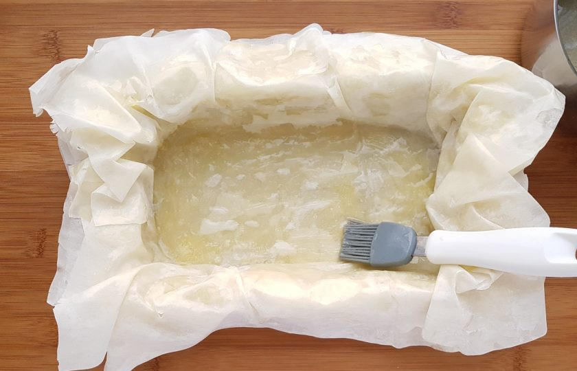 1. Этап. Рыбный пирог с тестом фило: Форму для выпечки застелите пергаментом, смазанным маслом. В форму выложите внахлест несколько листов теста так, чтобы края свободно свисали. Каждый лист смажьте растопленным сливочным маслом.