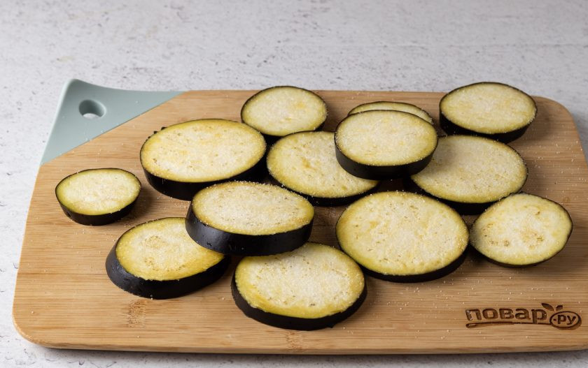 1. Этап. Холодная закуска из баклажанов с помидорами и чесноком: Баклажаны нарежьте кружочками толщиной 0,5 см. Посыпьте солью и оставьте на 15 минут, чтобы они пустили сок. После сполосните их в воде, обсушите с помощью бумажных полотенец и смажьте растительным маслом.