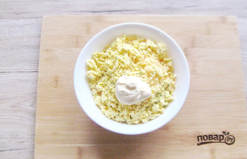 1. Этап. Яйца фаршированные крабовыми палочками и сыром: Яйца отварите вкрутую, охладите и разрежьте вдоль на половинки. Желтки аккуратно достаньте, разомните вилкой и добавьте в миску к крабовым палочкам и сыру с зеленью. Половинки белков отложите в сторону. Сюда же, в миску добавьте майонез. Солите по необходимости, учитывая солёность сыра и крабовых палочек. Тщательно перемешайте все ингредиенты с майонезом.