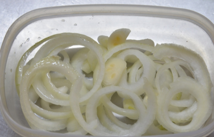 1. Этап. Рулетики из сельди в маринаде: Белый репчатый лук очистите, вымойте в воде и затем нарежьте кольцами. Слегка сбрызните его уксусом.