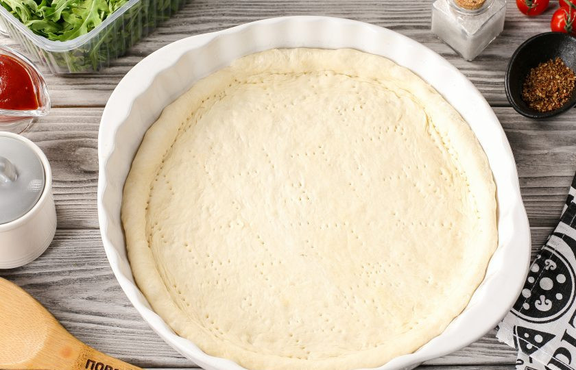 1. Этап. Пицца с рыбой: Рабочую поверхность присыпьте рукой и раскатайте тесто в форме круга. В зависимости от диаметра пиццы, будет зависеть и толщина готового теста. Рекомендую не менее 27-29 см., можете конечно раскатать больше или меньше. Переложите тесто на пергамент или в смазанную маслом жаропрочную форму. Руками сформируйте бортики, дно наколите вилкой, чтобы оно в процессе не вздувалось.