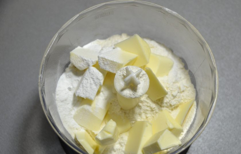 1. Этап. Пирог с зеленым луком и творогом: Положите в блендер 2/3 муки от общего объема, порезанное на кубики холодное сливочное масло. Добавьте соль и разрыхлитель для теста.