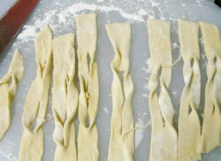 1. Этап. Хворост тонкий хрустящий на кефире: Посыпаем стол мукой. Берем скалку. Раскатываем тесто, присыпая его мукой, чтобы не прилипало. Раскатываем до минимальной толщины. После чего нарезаем ножиком на широкие пластины. Эти же пластины надрезаем посередине. Выворачиваем пластинки через надрезы, чтобы получились завитки.