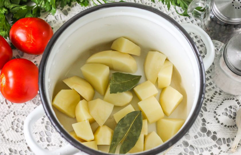 1. Этап. Борщ с болгарским перцем: Картофель очистите от кожуры, промойте клубни в воде, срезая поврежденные участки, нарежьте средними кубиками в кастрюлю. Добавьте туда же лавровые листья, влейте воду и поместите емкость на плиту. Отварите на среднем нагреве с момента закипания примерно 15 минут.