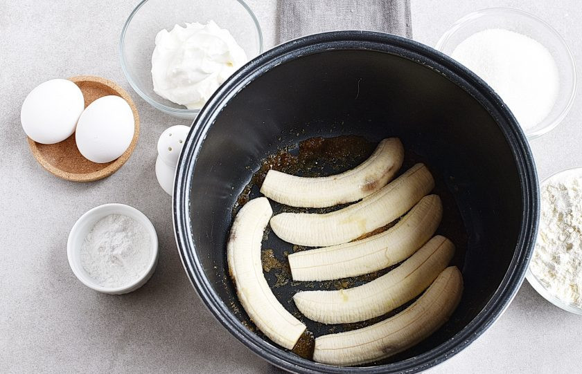 1. Этап. Банановый пирог в мультиварке: На дно мультиварки равномерно насыпьте коричневый сахар и слегка сбрызните его водой. Выложите сверху очищенные и разрезанные вдоль бананы – три штуки.