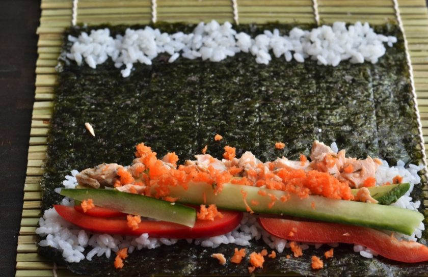 1. Этап. Суши с форелью: 2. Нарежьте тонкими ломтиками перец и огурец, на мелкой терке натрите морковь, разберите рыбу на кусочки. Разложите лист нори и на одну сторону выложите немного риса, затем перец и огурец, рядом положите вдоль рыбное филе, добавьте немного тертой моркови, а на другой край положите немного риса.