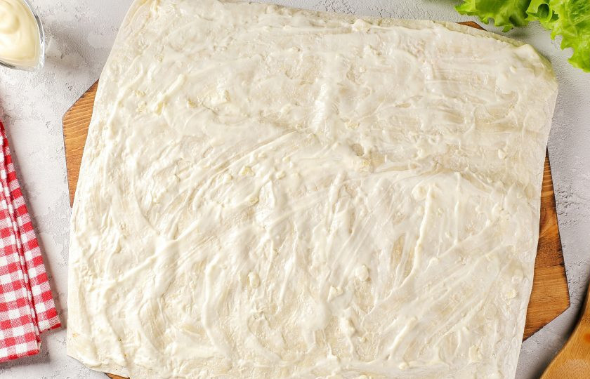 1. Этап. Лаваш с семгой: Соедините сметану и майонез. Добавьте давленый чеснок и перемешайте. Намажьте первый лаваш полученным соусом.