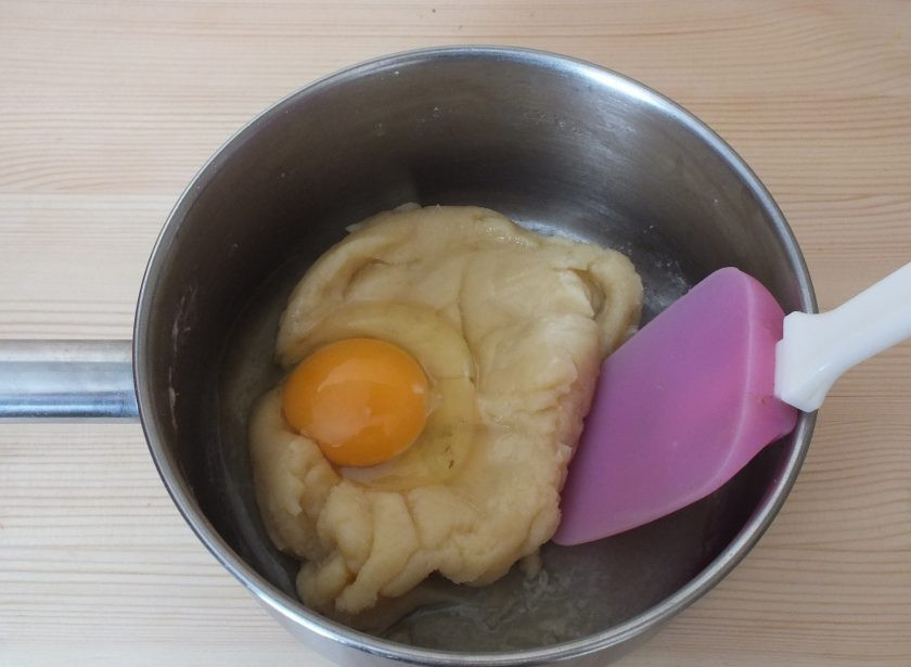 1. Этап. Профитроли с курицей: Когда тесто соберется в однородный комок, слегка его охладите (3-4 минуты) и добавьте яйца. По одному. После каждого яйца тщательно размешайте.