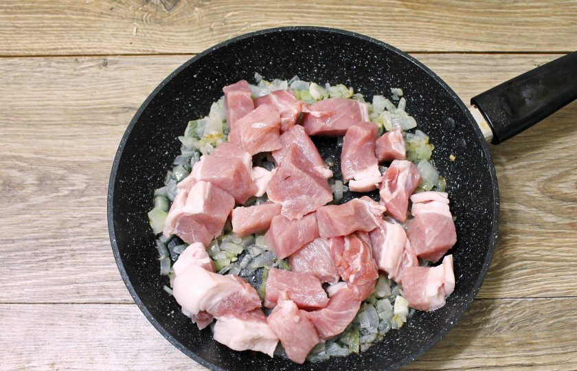 1. Этап. Мясо с баклажанами в горшочках в духовке: Свинину сполосните, обсушите и порежьте кубиком размером 1*1 сантиметр. Выложите мясо в сковороду с луком и перемешайте.