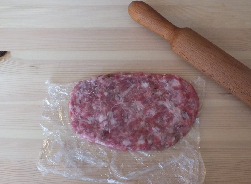 1. Этап. Лепешки из фарша: 3. Возьмите пищевую пленку. Положите на один край пленки подготовленную часть фарша, накройте вторым краем пленки и раскатайте в тонкую лепешку с помощью скалки.