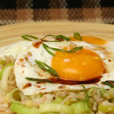 1. Этап. Жареный рис с имбирем: 3. Пока рис готовится, нагреть 1 чайную ложку масла в средней сковороде с антипригарным покрытием на среднем огне. Разбить яйца в отдельные небольшие миски. Добавить яйца в сковороду, посолить, накрыть крышкой и жарить до тех пор, пока белки не загустеют, а желтки не будут оставаться мягкими, от 6 до 8 минут. Разделить рис между сервировочными тарелками. Выложить сверху жареные яйца и полить соевым соусом и кунжутным маслом. Посыпать нарезанным зеленым луком и сразу же подавать.