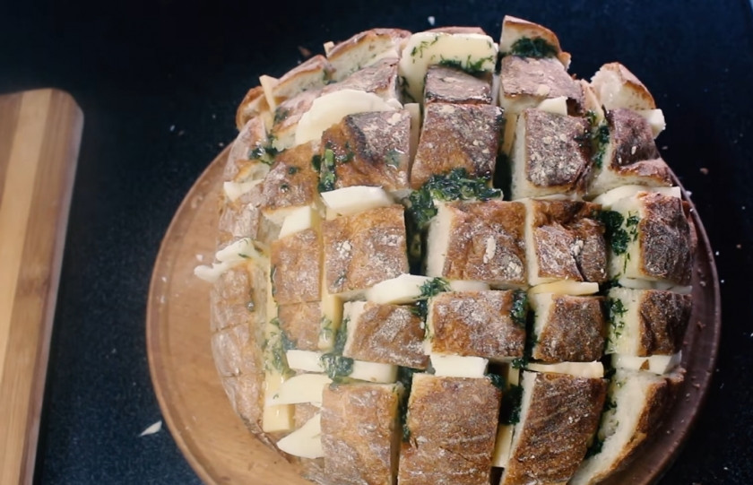 1. Этап. Закусочный хлеб с сыром и зеленью: 3. Сделайте надрезы вдоль и поперек хлеба, не дорезая до конца, и наполните эти разрезы начинкой. Старайтесь равномерно распределять сыр внутри разрезов. Залейте в разрезы сливочное масло с зеленью.